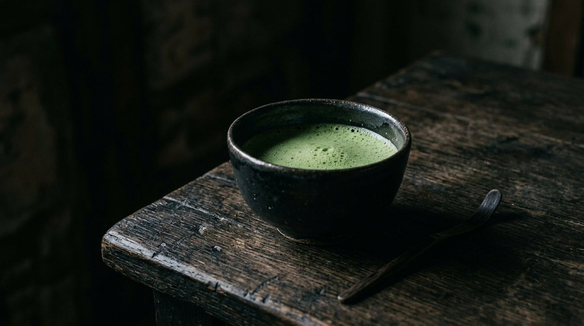 Taza oscura de matcha sobre mesa de madera con luz tenue y sombras profundas